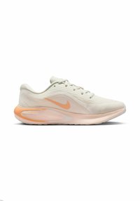 Chaussure de course Nike beige clair avec des accents de semelle pêche et un logo swoosh orange, vue de côté sur fond blanc.