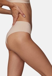 Sous-vêtements beiges sans coutures avec une taille haute, texture lisse et design minimaliste, mettant en valeur les hanches et les cuisses.