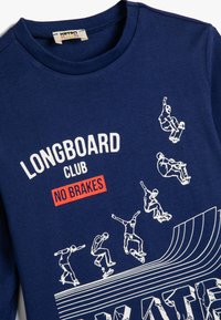 Granatowy sweatshirt wykonany z bawełny, z okrągłym dekoltem, białą grafiką skaterów oraz czerwoną napisą "LONGBOARD CLUB NO BRAKES."