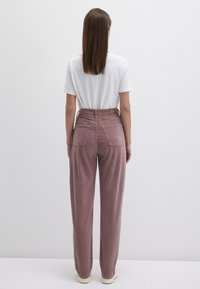 Helle rosa Cordhosen mit hohem Bund, Front- und Gesäßtaschen sowie einem strukturierten Stoffdesign, kombiniert mit einem schlichten weißen T-Shirt.