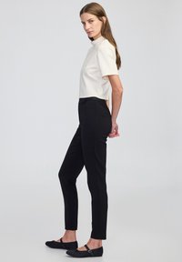 Haut crème à manches courtes avec un col haut, associé à un pantalon noir ajusté et des ballerines noires. Design simple, épuré et silhouette moderne.