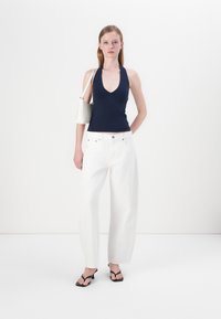 Mornarski halter top, bijele široke traperice s kopčanjem, crne sandale na petu i torba svijetle boje s dekorativnim detaljima.