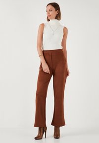 Weißes, geripptes, ärmelloses Rollkragenoberteil kombiniert mit braunen, samtigen, weitgeschnittenen Hosen und braunen, hochhackigen Ankle-Boots. Schlichte Schmuckakzente.