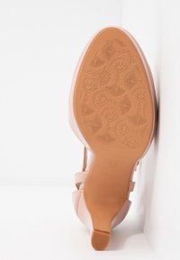 Sandale à talons hauts rose avec une tige lisse, bout ouvert et des straps décoratifs. La semelle en caoutchouc texturé présente un motif floral complexe. Taille 37.