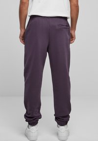 Lila joggers i mjukt material med elastisk midja, avsmalnande muddar och en liten bakficka. Bärs med vita sneakers.