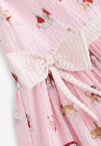 Tela rosa texturizada con perros impresos que llevan atuendos rojos y un gran lazo blanco con rayas rosas.