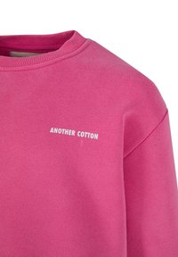 Różowa bluza z bawełny, z okrągłym dekoltem i ściągaczami przy rękawach. Napis "ANOTHER COTTON" na przodzie w kolorze białym. Gładka tekstura.