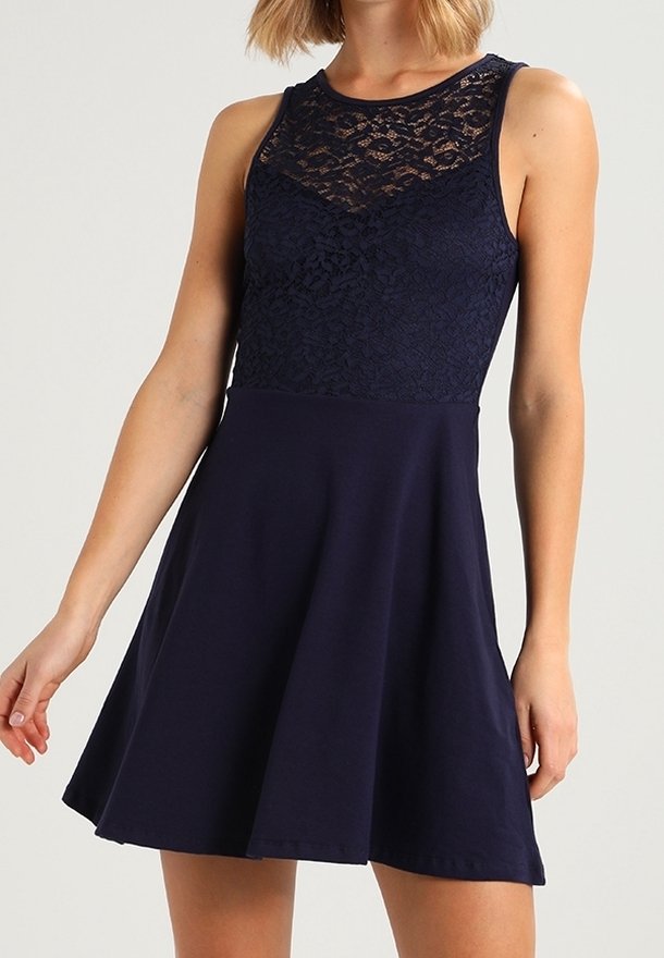 Robe bleu marine sans manches avec corsage en dentelle et encolure ronde, taille marquée et jupe évasée portée par une femme debout.