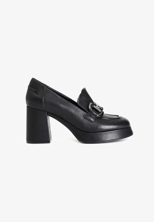Zapatos de tacón alto de cuero negro con punta redondeada, tacón cuadrado y detalle decorativo de hebilla en el empeine. Textura suave y diseño minimalista.