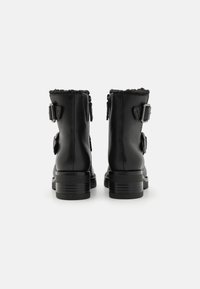 Botas de tobillo de cuero negro con un acabado texturizado, doble hebilla lateral, cuello acolchado y tacones gruesos y apilados. Cierres de cremallera a cada lado.