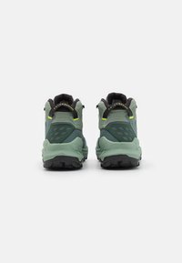 Scarpe da trail verdi con tomaia testurizzata, accenti neri, suola in gomma e lugs prominenti per la trazione. Presentano un motivo cucito sul lato.
