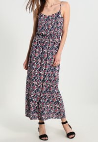 Robe longue fleurie bleu marine avec des fleurs rouges et blanches, dotée de fines bretelles, d'une taille élastique et d'une silhouette fluide.
