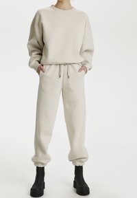 Felpa in cotone beige con collo rotondo e vestibilità comoda, abbinata a pantaloni jogger affusolati coordinati con vita elastica e polsini.