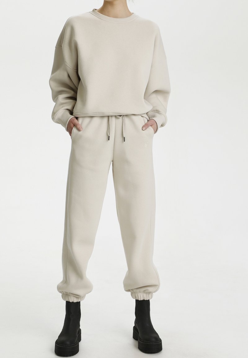 Felpa in cotone beige con collo rotondo e vestibilità comoda, abbinata a pantaloni jogger affusolati coordinati con vita elastica e polsini.