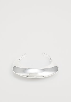 Bracelet en métal argenté avec un design lisse et courbé, doté d'une surface polie et d'extrémités ouvertes pour un ajustement réglable. Apparence minimaliste et élégante.