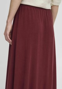 Fustă maxi burgundă, realizată dintr-un material moale și ușor, cu un brâu elastic și un design fluid, evidențiind o textură netedă și linii curate.