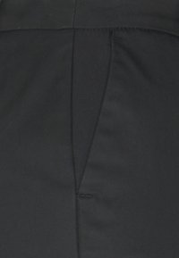 Czarna tkanina o gładkiej fakturze, z centralnym zagięciem i dyskretnym przeszyciem wzdłuż pasa i szwów.