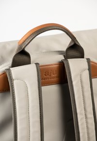 Gray fabric backpack featuring brown leather accents, padded shoulder straps, and a top handle. Minimalist design with stitched details.