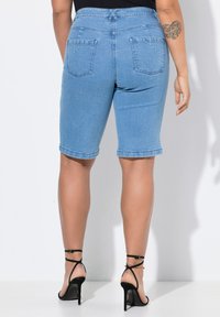 Bermudas de mezclilla en color azul claro con tiro medio, corte recto y bolsillos traseros. Combinadas con unos tacones altos negros con tiras.
