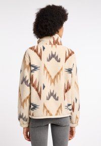 Cremfarbene Fleecejacke mit geometrischen Mustern in Braun-, Blau- und Grautönen. Mit hohem Kragen und elastischen Bündchen. Bequeme Passform.