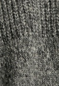 Tissu tricoté gris présentant un motif texturé avec des nuances variées. Le matériau semble doux, avec des fils flous et un aspect naturel, organique.