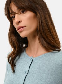 Světle modrý kardigan vyrobený z měkké, texturované tkaniny. Má kulatý výstřih a zapínání na knoflíky, s pohodlným střihem v oblasti ramen.