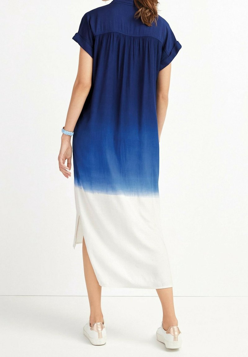 Femme portant une robe midi à manches courtes ombrée du bleu vers le blanc avec une fente latérale, associée à des baskets blanches, vue de dos.