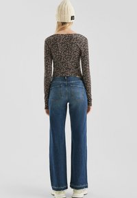 Langarm, zwart bloemetjes top in combinatie met hoge taille, brede blauwe jeans. Model draagt een gebreide crèmekleurige beanie en witte sneakers.