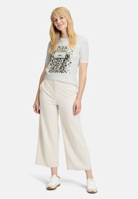 Lys grå t-shirt med leopardprintdesign og et rektangulært mærke. Parret med cremede bukser med bred ben og hvide sneakers.