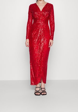 Femme portant une longue robe rouge en sequins à manches longues, décolleté en V, et fente avant, associée à des sandales noires à lanières.