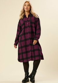 Abito camicia in flanella a maniche lunghe con un motivo a quadri viola e nero, chiusura frontale a bottoni e una vestibilità rilassata con spacchi laterali.