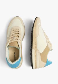 Beige and cream sneakers with suede and leather materials, featuring blue accents and black textured soles. Lace-up design, padded collar.