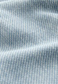 Tissu en denim bleu clair avec un motif sergé diagonal et des plis subtils créant des ombres douces et une texture.