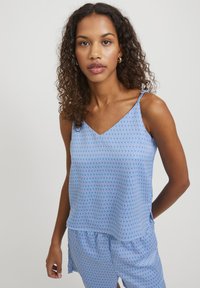 Ljusblå ärmlös topp med V-ringning, med ett vertikalt mönster av tunna, utspridda linjer i mörkare blått och lila. Mjuk, flödande tyg.