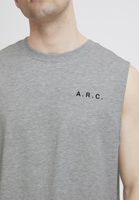 Pilkas be rankovių marškinėliai, pagaminti iš minkštos medžiagos, su apvaliu iškirpimu ir juodu užrašu "A.R.C." kairėje krūtinės pusėje.