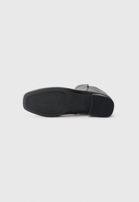 Bota de cuero negra tumbada de lado que muestra una suela de goma cuadrada con un agarre texturizado y un tacón bajo.