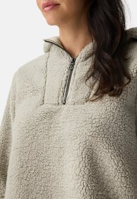 Crème fleece pullover met een half-rits ontwerp, gestructureerd oppervlak en een capuchon. Heeft een minimalistische zak aan de voorkant.