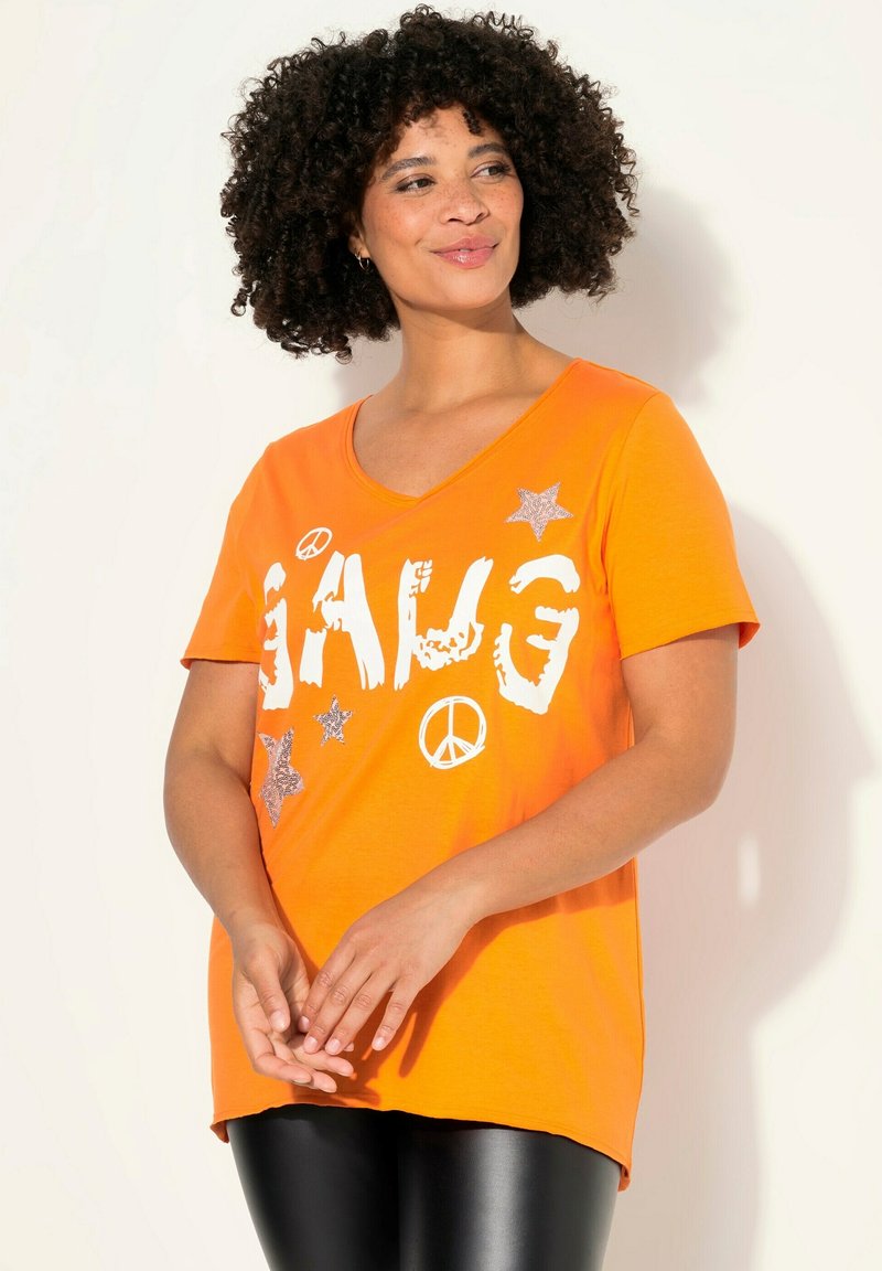 Orange bomulds T-shirt med V-udskæring, der har hvid tekst "GANG", fredstegn og sølvstjernedetaljer. Korte ærmer og afslappet pasform.