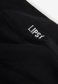 Gros plan d'un tissu noir avec des coutures visibles et un logo "LIPSY" argenté brillant.