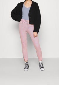 Cardigan negro de punto, top sin mangas azul claro, jeans rosa de tiro alto con botones en la parte delantera y zapatillas negras de caña alta.