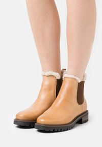 Bottes à cheville en cuir fauve avec une finition lisse, doublure en peau de mouton, panneaux élastiques latéraux et semelle en caoutchouc texturée pour une meilleure adhérence.