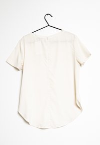 Kurzärmelige, hellcremefarbene Bluse mit abgerundetem Saum, Knopfverschluss im Rücken und glatter, leicht glänzender Stoffstruktur.