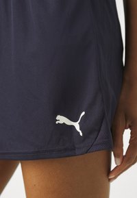 Tengerészkék sportnadrág, fehér Puma logóval. Az anyag sima, légáteresztő hálós oldalpanellel és lazán illeszkedő fazonnal rendelkezik.