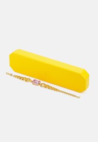 Brățară din lanț de aur, cu o piatră prețioasă roz rectangulară, așezată lângă o cutie octogonală galbenă strălucitoare. Textură netedă și finisaj lustruit.