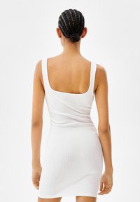 Robe blanche à côtes, avec un dos carré, une coupe ajustée et des bretelles larges, se distinguant par une texture lisse et une longueur mi-cuisse.