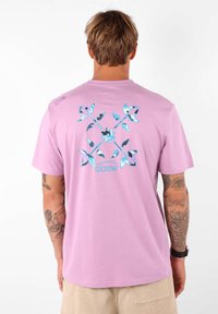 T-shirt rose clair en coton avec un design graphique comportant des accents et des formes bleues au dos ; manches courtes et coupe décontractée.
