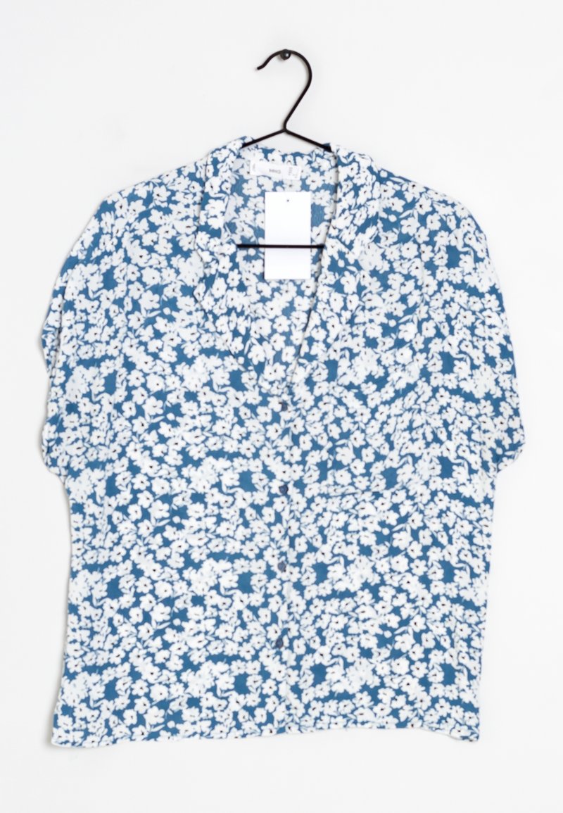 Blouse bleu à manches courtes avec un motif floral blanc, accrochée sur un cintre noir, contre un fond blanc.