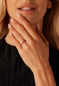 Silberring mit mehreren blauen Edelsteinen, getragen an einer Hand mit heller Nagellackierung, vor einem strukturierten schwarzen Hintergrund.