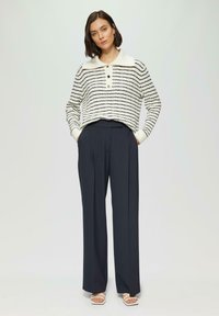Pull à motif rayé en blanc et bleu marine, avec un col plat et trois boutons. Associé à un pantalon large taille haute bleu marine.