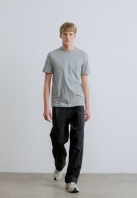 Szürke, rövid ujjú póló kerek nyakkivágással és kontrasztos szegéllyel, laza fekete nadrággal és világos színű tornacipővel párosítva.